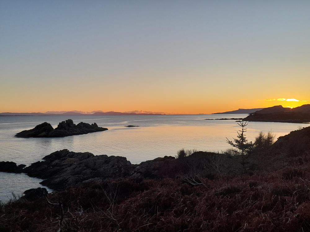 Sunset over Dragon Island seen from Rubha Phoil on the Isle of Skye, casting golden light across the sea in a magical, dreamlike coastal landscape